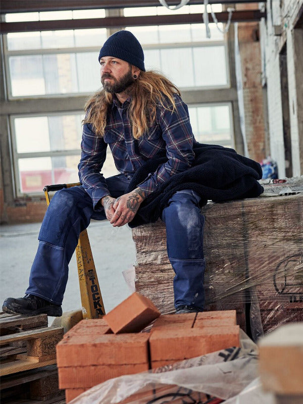 Person i arbetskläder på byggarbetsplats - slitstarka kläder från Jobbutrustning.se