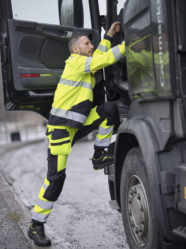 Person i varselkläder kliver upp i lastbilens hytt via fotsteg – säkerhet och ergonomi i fokus.