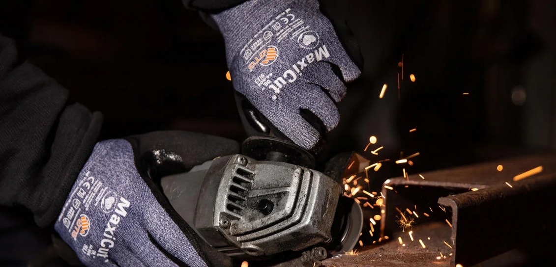 Person med skyddshandskar använder vinkelslip på metall – gnistor flyger, säkerhetsutrustning i fokus.